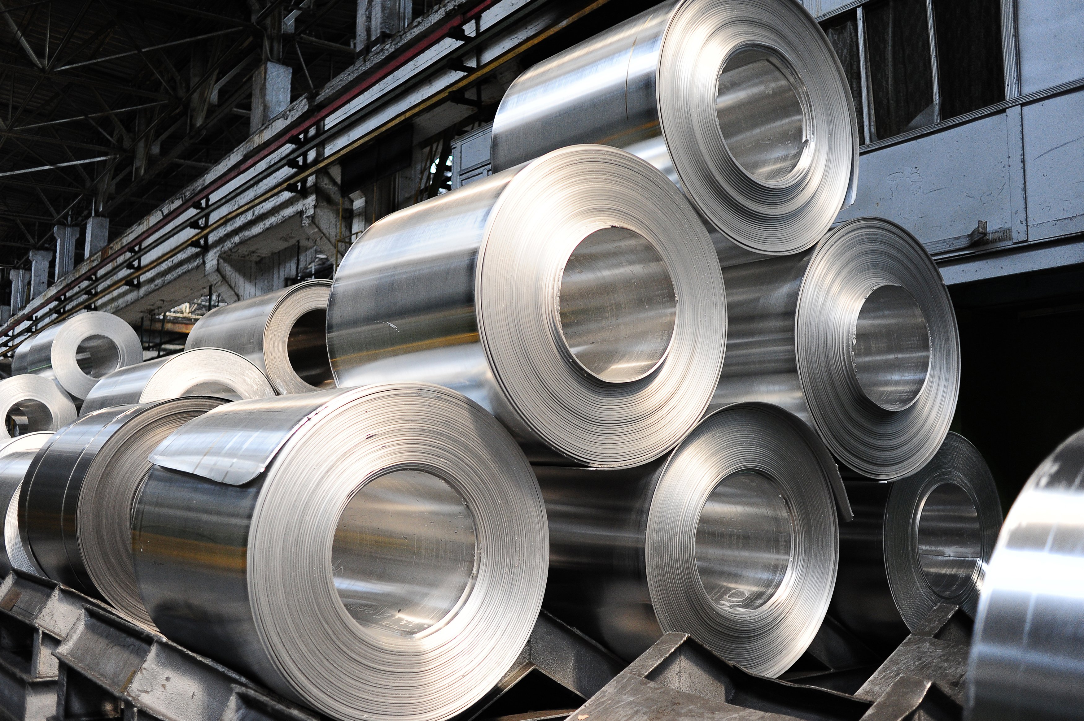 A large group of rolled aluminum sheets stacked in a factory setting, showcasing various aluminum products for manufacturing.
